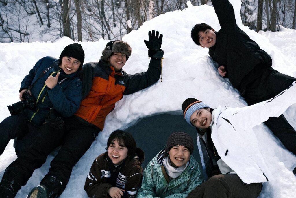 かまくらの前で笑顔の若者たち