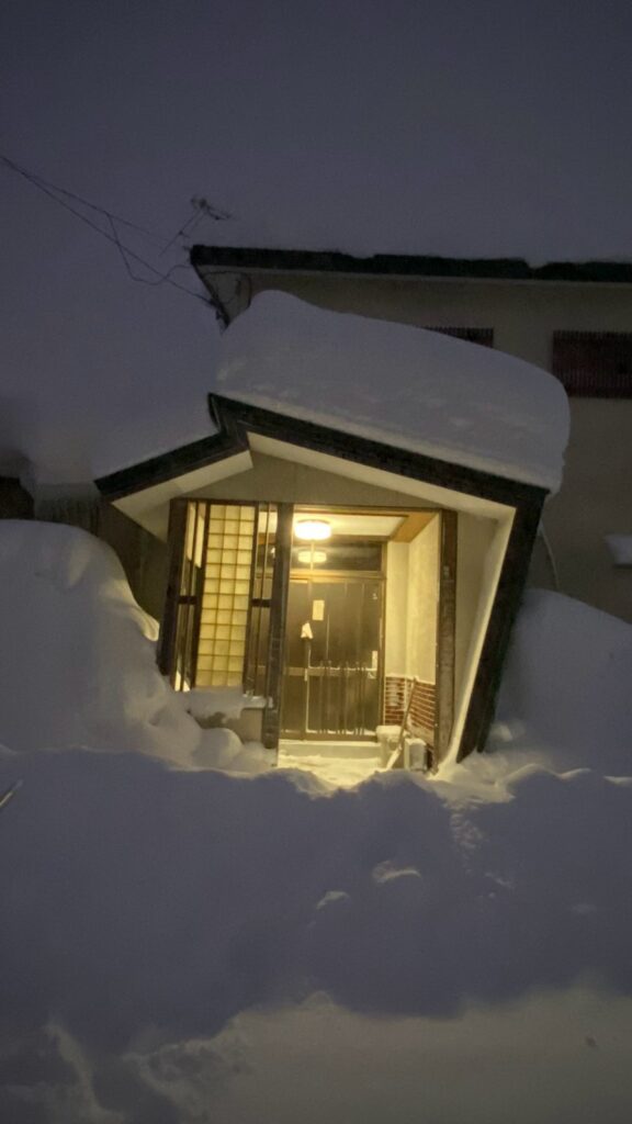 雪に包まれた冬の夜、明かりの灯る玄関